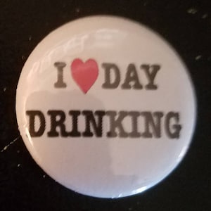May include: White button with a red heart and the text "I ♥ DAY DRINKING" in black.