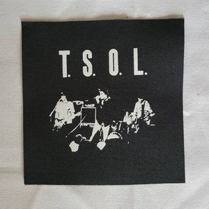 May include: Black and white patch with the text "T.S.O.L." in white lettering. The patch features a silhouette of a band playing music.