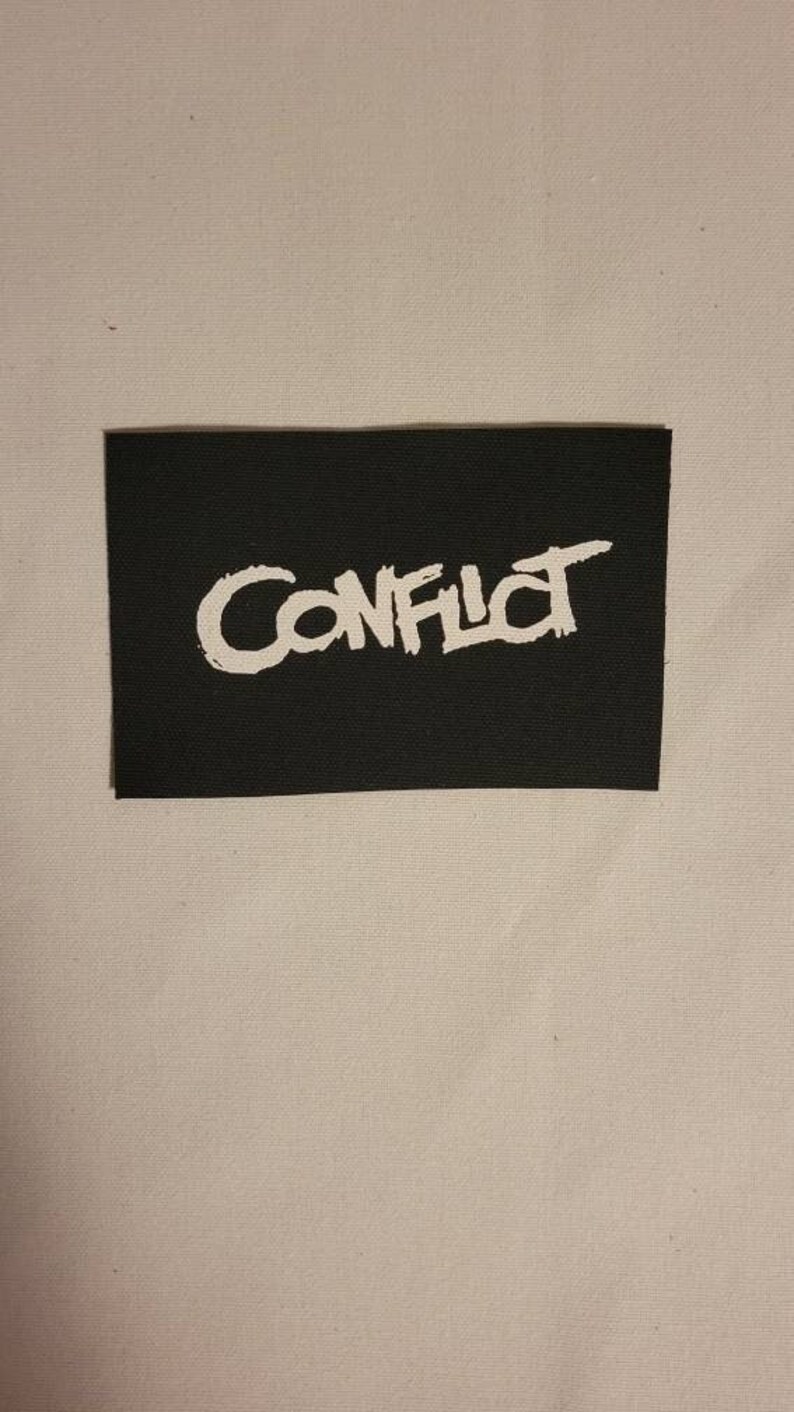 May include: Black fabric patch with white lettering that reads "CONFLICT" in a stylized font.