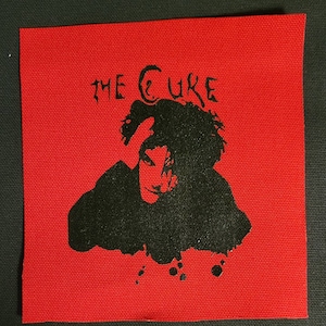 Puede incluir: Parche termoadhesivo en blanco y negro con una silueta de una persona con el texto "THE CURE" sobre la imagen. El parche est&aacute; sobre un fondo rojo.