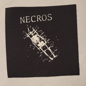 Może przedstawiać: Czarno-biała naszywka haftowana z napisem "NECROS" w białych literach i szkieletem w klatce.