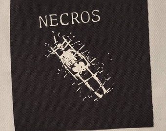May include: Black and white embroidered patch with the word "NECROS" in white lettering and a skeleton in a cage design.