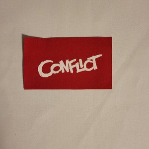 May include: Red fabric patch with white lettering that says "CONFLICT" in a stylized font.