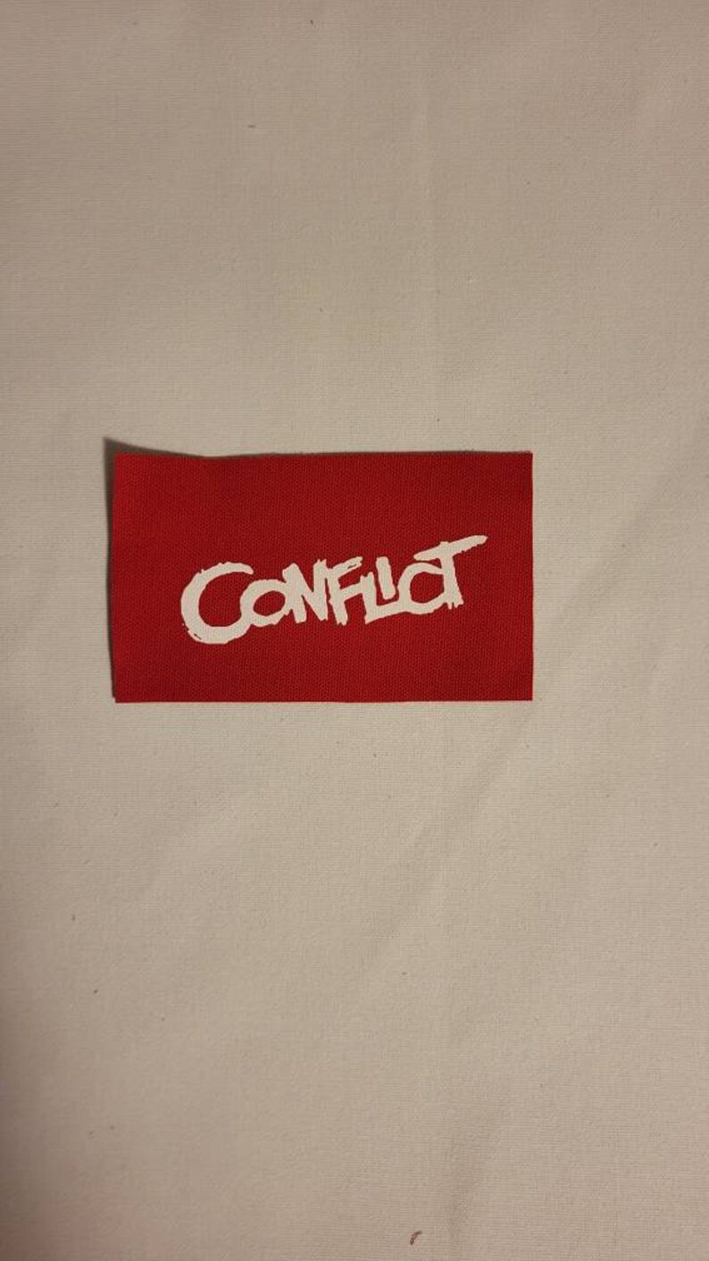 May include: Red fabric patch with white lettering that says "CONFLICT" in a stylized font.