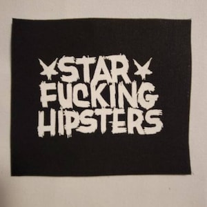 Może przedstawiać: Czarna prostokątna naszywka z napisem "STAR FUCKING HIPSTERS" w białej, stylizowanej, postarzanej czcionce. Słowo "STAR" ma po bokach grafikę gwiazdy. Naszywka znajduje się na białym tle.