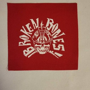 May include: Red fabric patch with a white skull wearing a helmet and the words "Broken Bones" in a circular design.