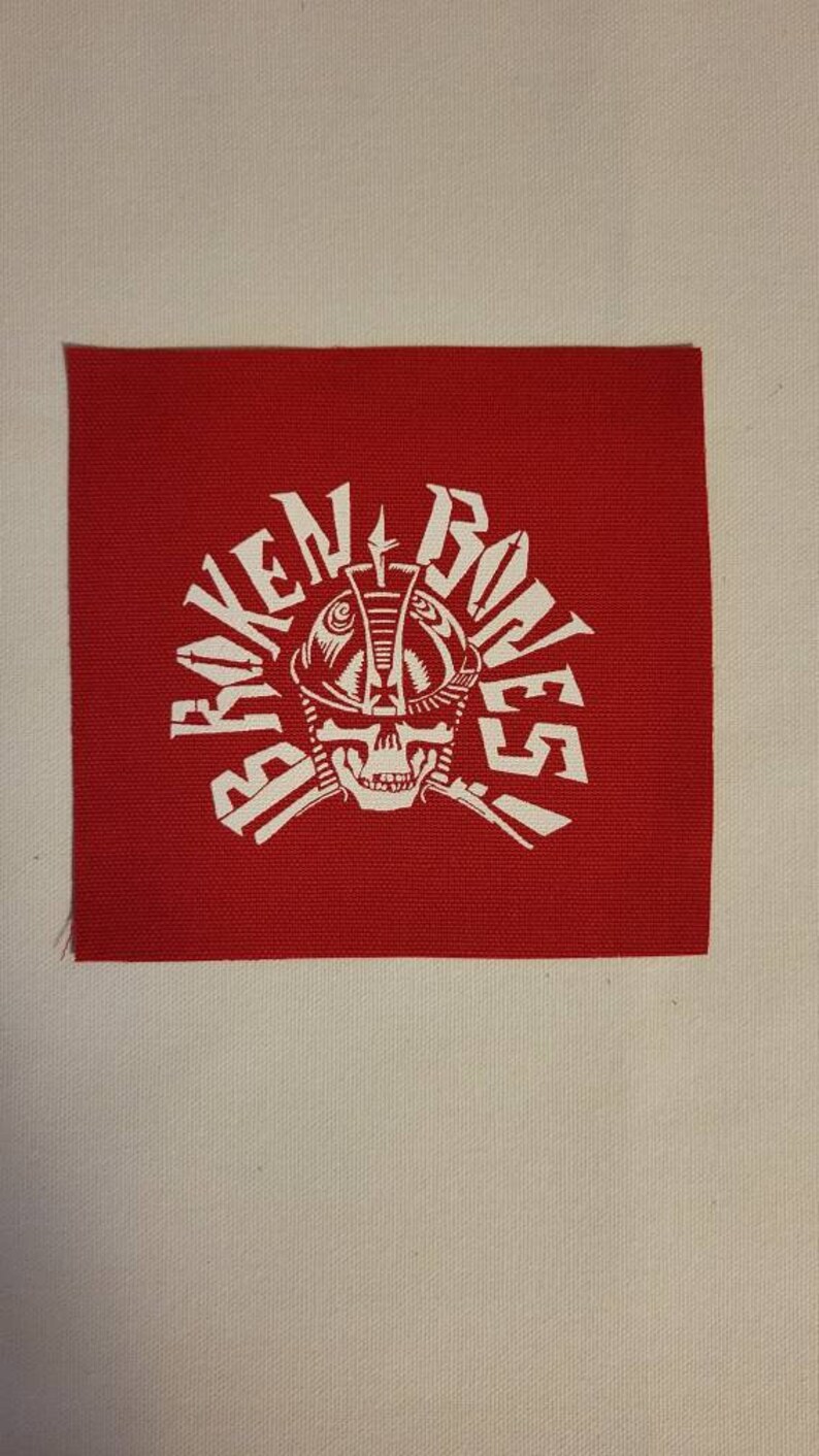 May include: Red fabric patch with a white skull wearing a helmet and the words "Broken Bones" in a circular design.