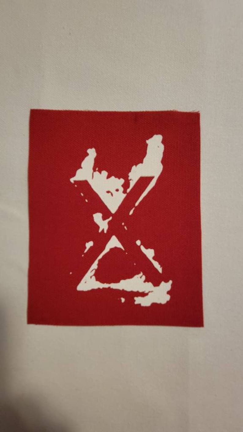 Op de afbeelding: Rode stoffen patch met een witte X in een verweerde stijl.