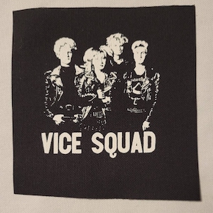 May include: Black and white image of a band called "Vice Squad" with four members wearing leather jackets. The band members are standing in a row, with the lead singer in the centre.