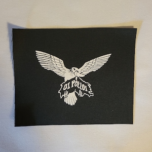 以下が含まれることがあります： 白い鷲が「Oi Polloi」と書かれたバナーを持っている黒い布のパッチです。