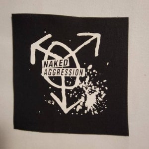 May include: Black and white patch with a stylized graphic of arrows and a circle with the text "NAKED AGGRESSION" inside.