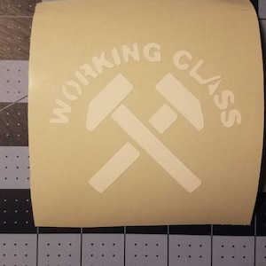 May include: A beige vinyl sticker with the text "WORKING CLASS" in white lettering, with a stylized image of two crossed hammers.