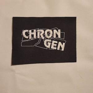 Könnte beinhalten: Schwarzer Stoff-Patch mit weißem Text, der "CHRON GEN" in einem rissigen, gebrochenen Schriftstil lautet.