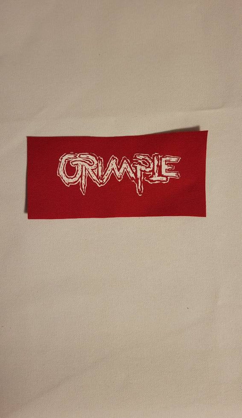 Op de afbeelding: Een rood stoffen patch met het woord "CRUMPLE" in witte, gestileerde letters.