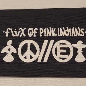 May include: Black fabric patch with white text and symbols. The text reads "Flux of Pink Indians." The symbols include a peace sign, a stylized "E" and two other symbols.