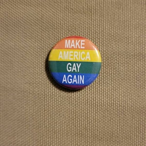May include: A rainbow-colored button with the text "Make America Gay Again" in white.