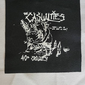 May include: Black and white patch with a graphic of a person holding a bottle and a glass. The text "The Casualties" and "40 oz. casualty" are printed on the patch.