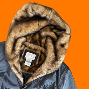 May include: A dark gray jacket with a faux fur-lined hood. The hood's interior features brown and tan faux fur. The jacket has a zipper closure and a tag that reads "WHITE STAG".