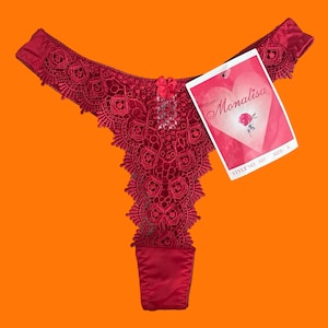 Pode incluir: Tanga vermelha de renda com um laço de cetim e uma etiqueta que diz "Monalisa" com uma rosa e o texto "Style No 101 Tamanho L".