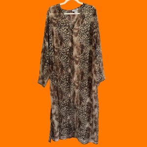 May include: A long-sleeved, sheer duster cardigan featuring a brown and black leopard print pattern. The garment has a V-neckline, a button-front closure, and vertical rows of small, shimmering metallic studs running down the front panels.
