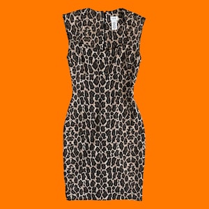 以下が含まれることがあります： 茶色、黒、タンの色合いのヒョウ柄模様のノースリーブシースドレス。 ドレスは丸いネックラインとフィットしたシルエットです。 ネックラインの近くに小さなタグが見えます。 オレンジ色の背景に表示されています。