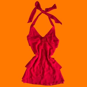 以下が含まれることがあります： 深いVネックライン、中央の布製ロゼットのディテール、複数の水平なフリル層が特徴の鮮やかな赤色のホルターネックトップス。首元には長い布製の紐があり、上部でリボン結びになっています。