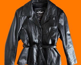 May include: A black leather jacket featuring a notched collar, long sleeves, and a front button closure. The jacket includes a matching tie belt at the waist and a black interior label with the white text maxima and Wilsons The Leather Experts.