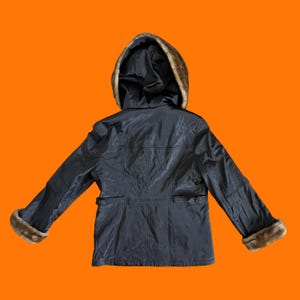 May include: A black jacket with a fur-lined hood and cuffs, displayed against an orange background. The jacket has a tailored fit with pockets and a belt detail at the waist. The fur trim is a light brown color.