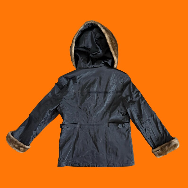 May include: A black jacket with a fur-lined hood and cuffs, displayed against an orange background. The jacket has a tailored fit with pockets and a belt detail at the waist. The fur trim is a light brown color.