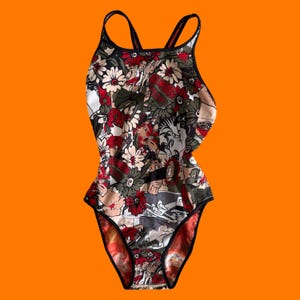 May include: One-piece swimsuit with a floral and comic book-style print. The swimsuit features a black trim, thin straps, and a low back. The print includes red, white, and beige flowers, along with comic book panels and text.