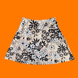 May include: A-line skirt with a beige background and a floral pattern in black and white. The skirt features a high waist and a flared silhouette, perfect for a casual or semi-formal look. The floral design includes various flower shapes and leaf patterns.