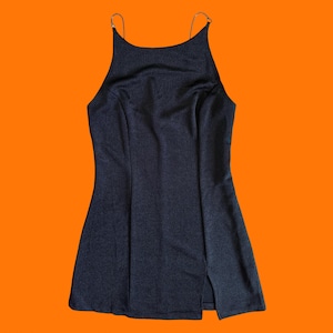 May include: A dark blue mini dress with thin, gold-colored straps. The dress has a high neckline and a slit on the left side. The background is a solid orange color.