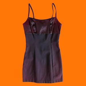 May include: A dark purple mini dress with thin spaghetti straps. The bodice is a darker shade of purple satin, and the lower portion is a slightly lighter shade of purple. The dress has a fitted silhouette and is likely made of a synthetic material.