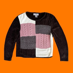 May include: A colour-block sweater in brown, white, pink, and grey. The sweater has a crew neck and long sleeves. The front panel has a cable knit design in pink and white. The sleeves are a dark brown corduroy material.