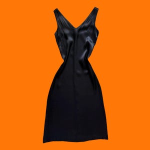 May include: A sleeveless black slip dress featuring a V-neckline and a smooth, satin-like finish. The garment has a fitted bodice that transitions into a straight, knee-length skirt, showcasing a fluid drape and a consistent dark black color throughout.