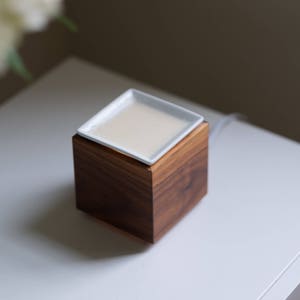 May include: A white ceramic dish sits on top of a wooden base, which is a diffuser for essential oils.