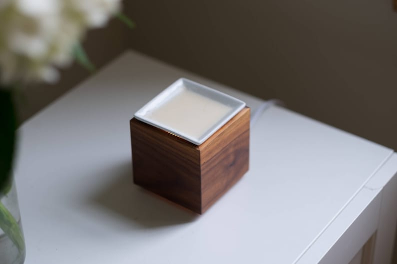 May include: A white ceramic dish sits on top of a wooden base, which is a diffuser for essential oils.