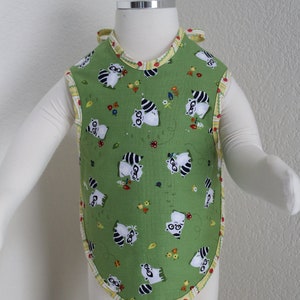 May include: Green baby bib with a yellow and white trim. The bib features a pattern of raccoons wearing glasses and holding flowers.