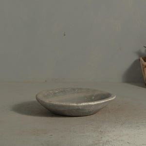 May include: A small, round, gray ceramic bowl with a textured surface. The bowl has a shallow depth and a slightly raised rim. The bowl is sitting on a gray surface.