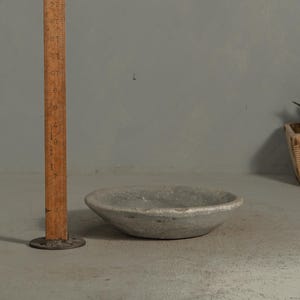 May include: A small, round, gray bowl with a rough texture. The bowl is approximately 6 inches in diameter. A wooden ruler stands next to the bowl, providing a size reference. The bowl sits on a gray surface.
