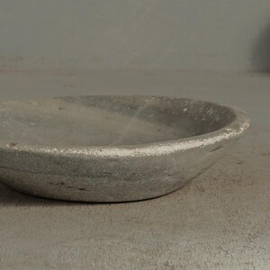 May include: A small, round, gray stone bowl with a slightly textured surface. The rim of the bowl has a white painted edge. The bowl is likely used for decorative purposes or for holding small items.