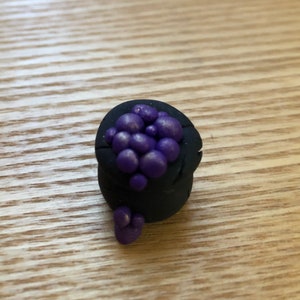 May include: A small black cauldron filled with purple beads. The beads are spilling out of the cauldron.