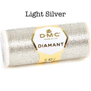 May include: A spool of DMC Diamant embroidery thread in light silver. The spool is labeled with the DMC logo and the words "Diamant" and "Fondee en 1746".