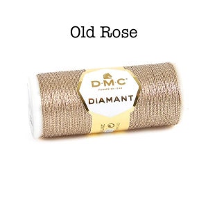 May include: A spool of DMC Diamant metallic embroidery thread in the color Old Rose. The thread is a shimmery gold color with a subtle pink hue.