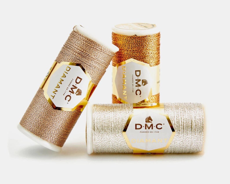 May include: Three spools of DMC Diamant metallic embroidery thread. The spools are gold, silver, and rose gold.