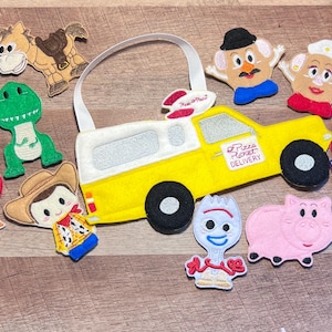 May include: A yellow felt Pizza Planet delivery truck bag with a white handle, surrounded by various embroidered felt character patches including a cowboy, cowgirl, space ranger, dinosaur, pig, spork, and other figures from a popular animated film.