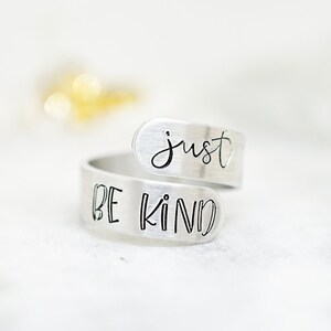 May include: A silver ring with the words "just be kind" engraved on it.