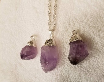 Könnte beinhalten: Drei Amethyst-Kristall-Anhänger an silbernen Ketten. Der größte Anhänger ist an einer längeren Kette und die beiden kleineren Anhänger sind an kürzeren Ketten.