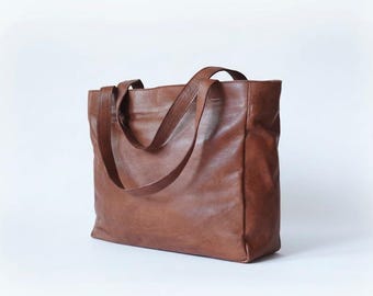 May include: A brown leather tote bag with two handles. The bag is rectangular with a spacious interior. The leather has a slightly distressed appearance, giving it a vintage look. The bag is suitable for carrying various items.