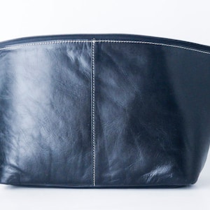 Puede incluir: Una bolsa de cuero negro con cremallera y costuras blancas. La bolsa está hecha de cuero suave y texturizado.